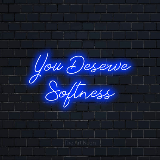 "You Deserve Softness" text design with neon effect on a black brick wall